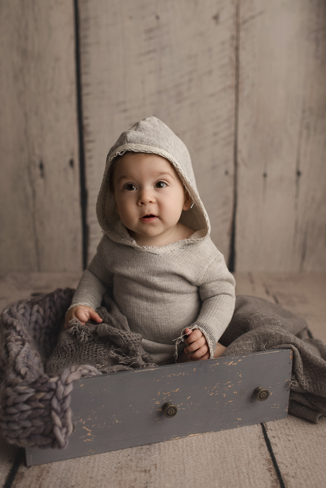 Wearing a cute hooded romper at his sitter milestone session.