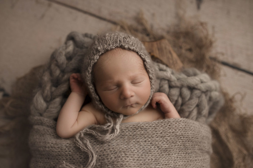 Sleeping baby boy posed in a trench with a grey blanket at his newborn photography session.