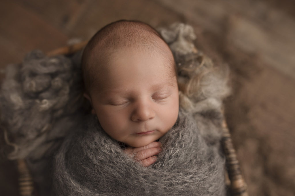 Handsome baby boy wrapped up and posed in a basket at his newborn photography session in Lafayette.