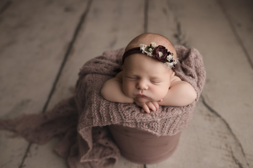 Adorable baby girl posed in a lavender bucket during her newborn photography session in Lafayette Indiana.