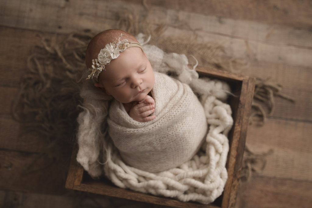 Posed newborn girl in a wooden crate at her Indiana newborn photography session.