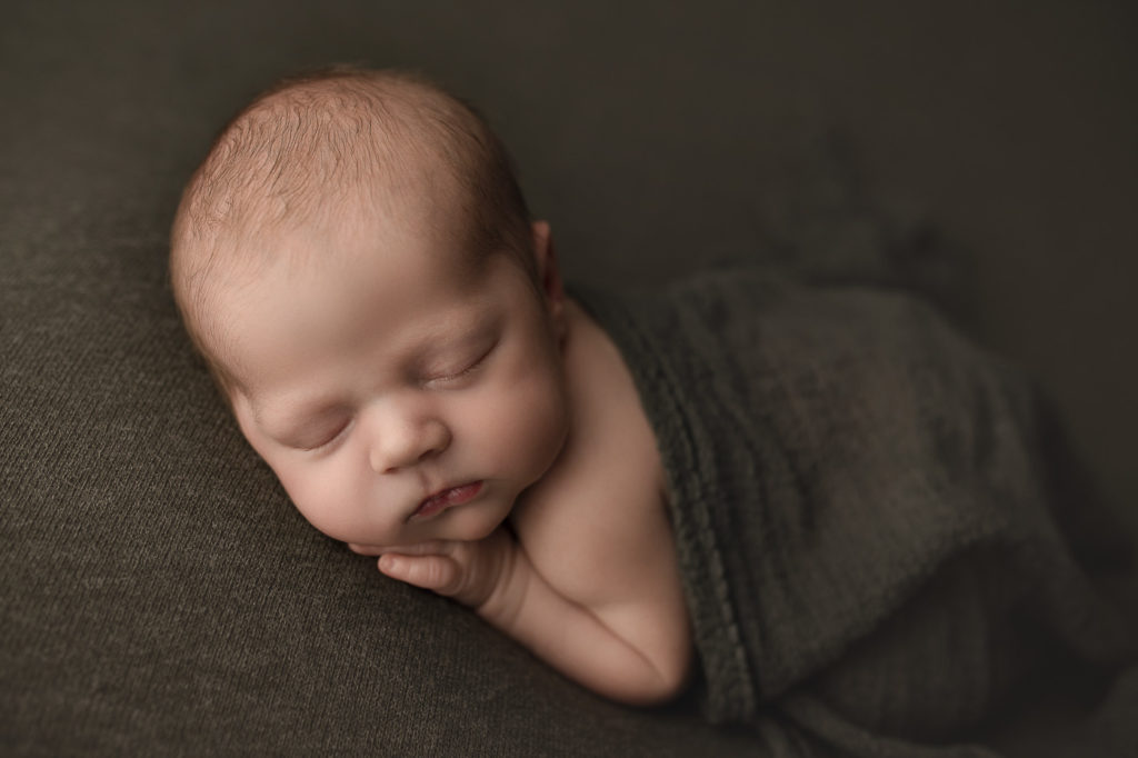 Cute baby boy in dark green backdrop during newborn session.