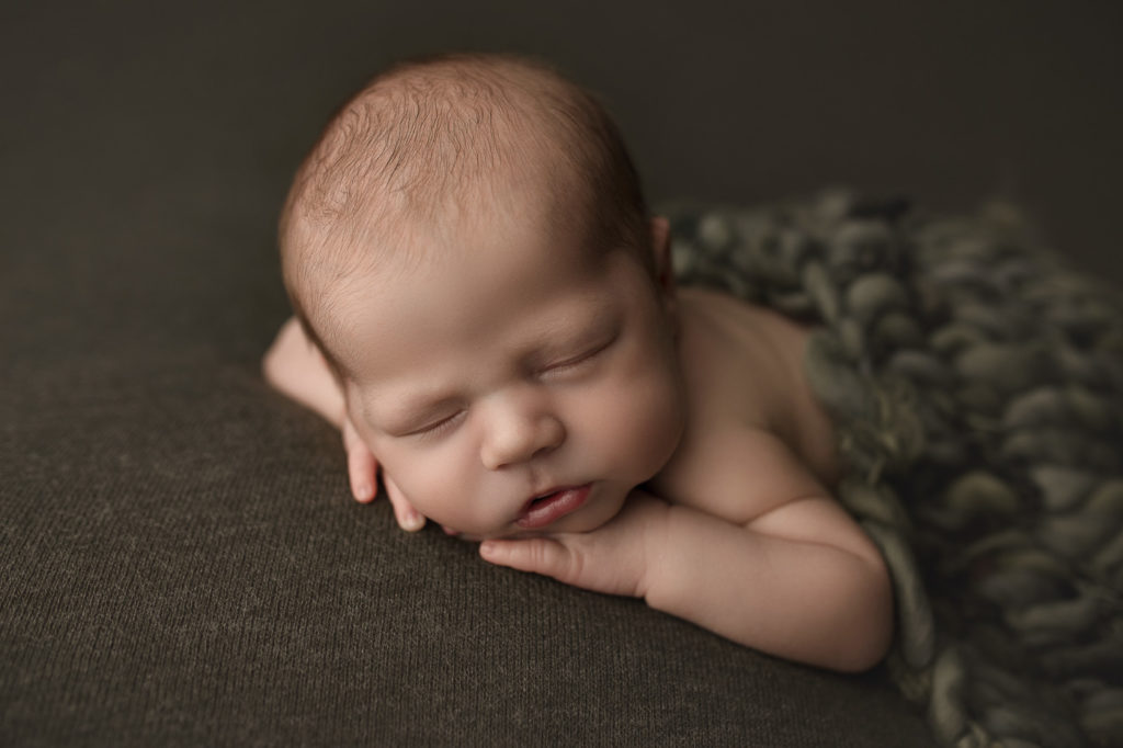 Handsome boy posed on a green fabric at his newborn photography session in Indiana.