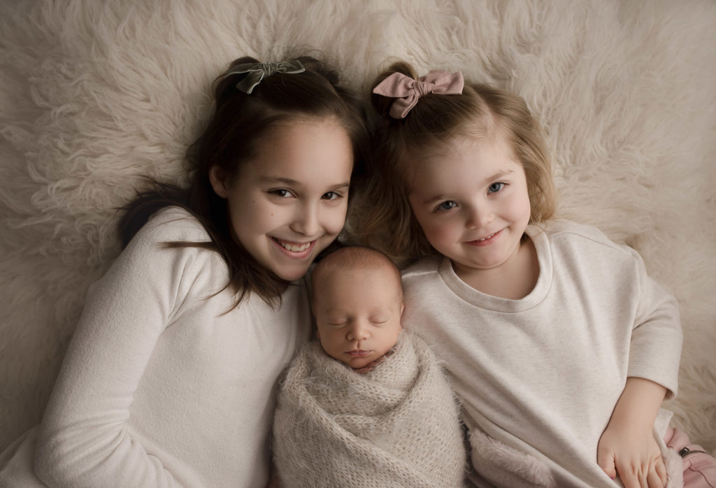 Cute sisters snuggling their brother during his newborn session in Lafayette Indiana.