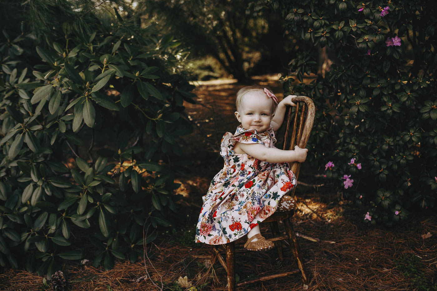Cute little girl sitting on a wooden chair at her milestone session.