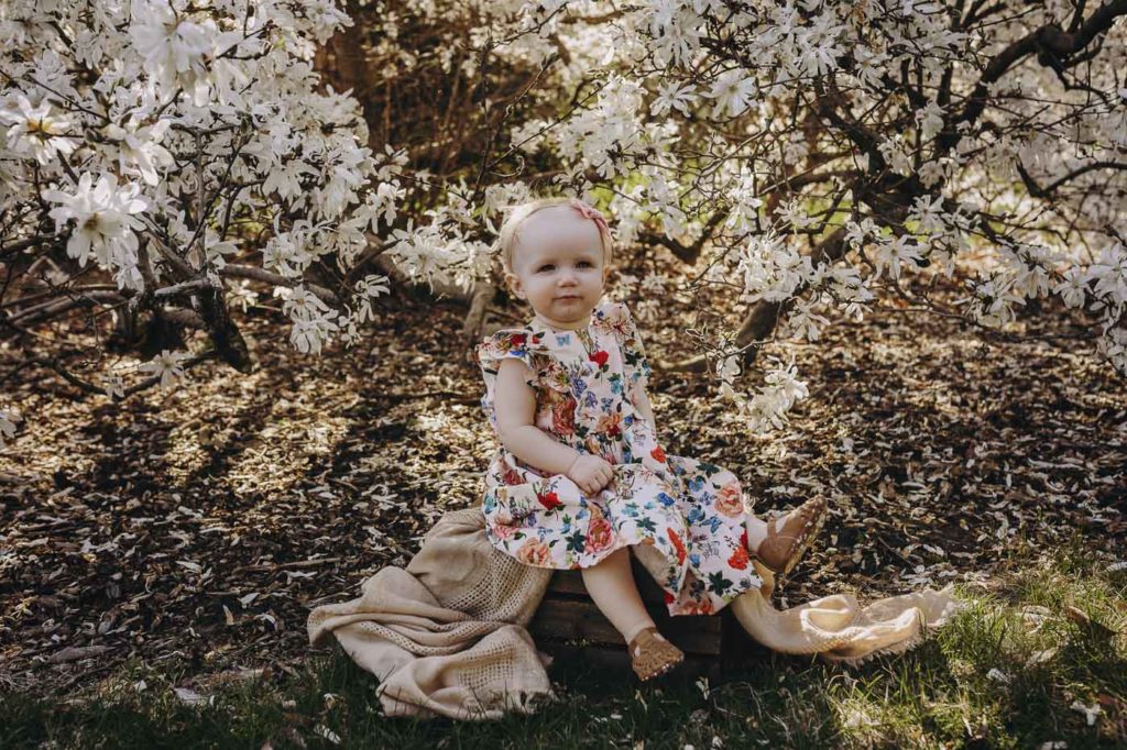 Sweet girl sitting under a tree with white blooms during her milestone session.