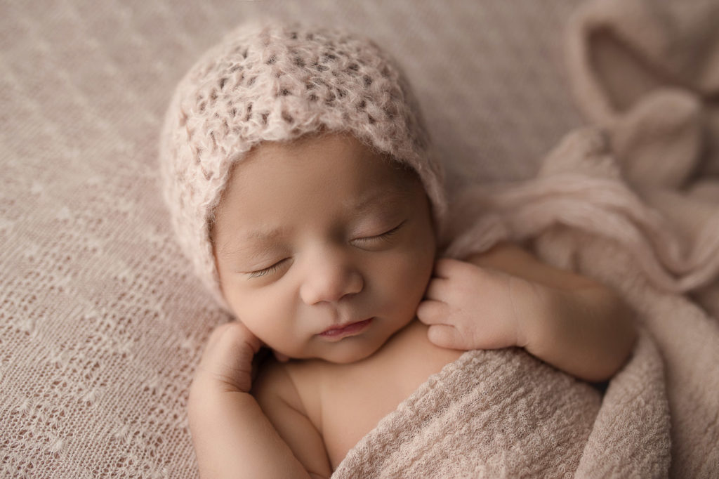 Sweet newborn girl wearing a pink bonnet for her newborn session in Indiana.
