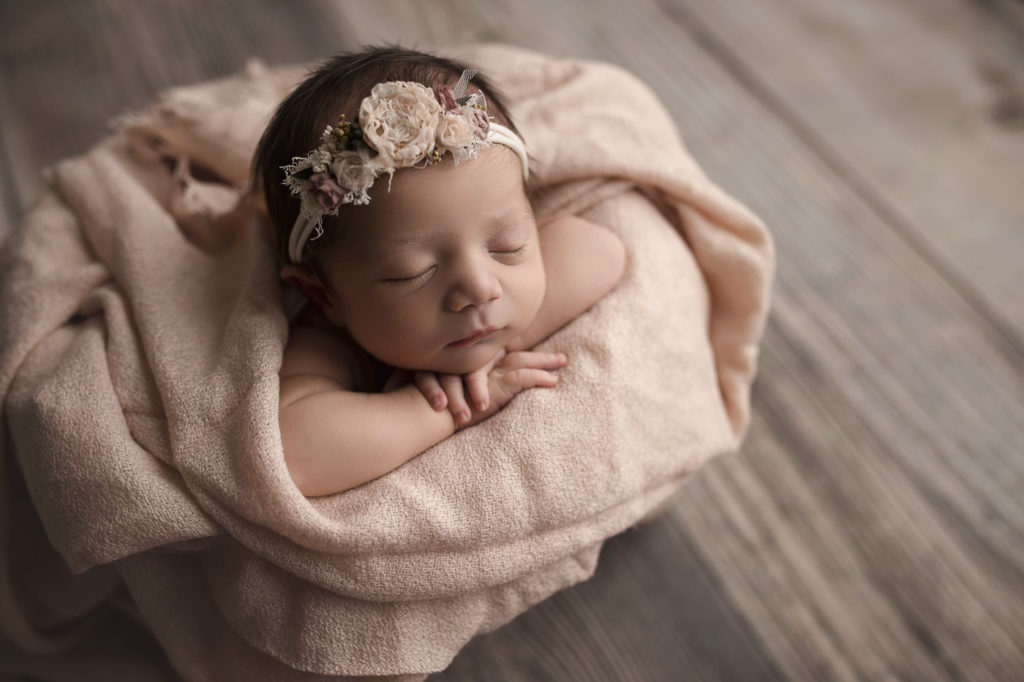 The sweetest baby posed in a bucket with pink accents during a studio newborn session.