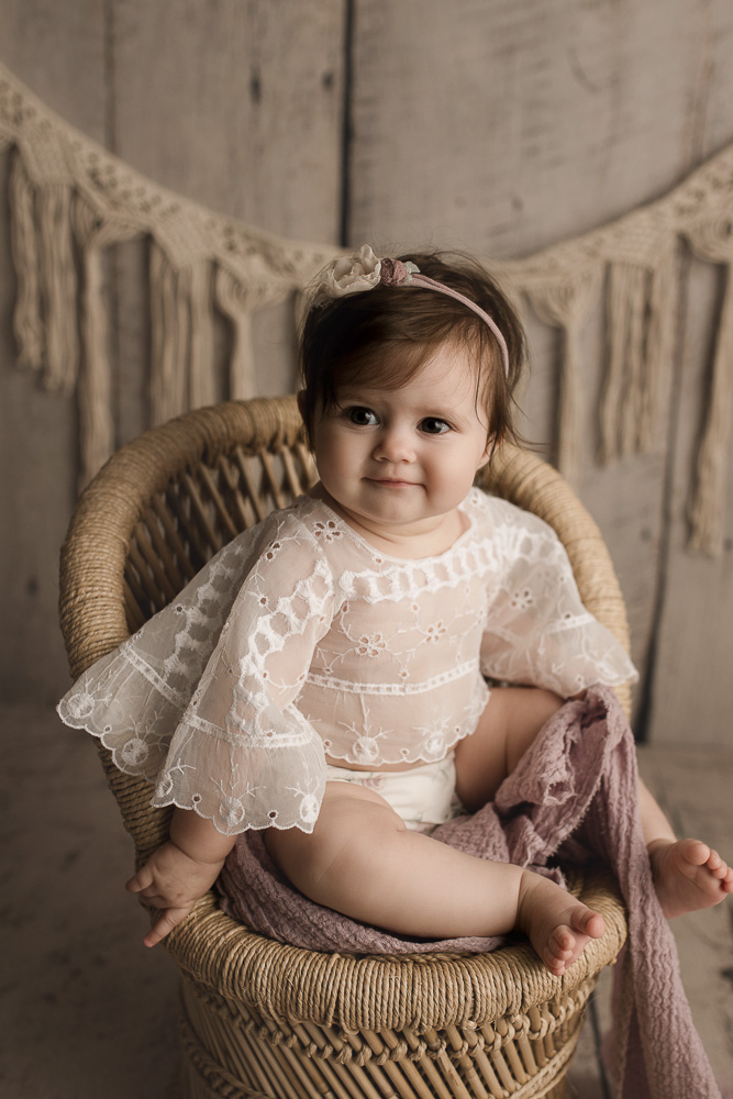 Cute baby girl sitting on a wicker chair during her photography session.