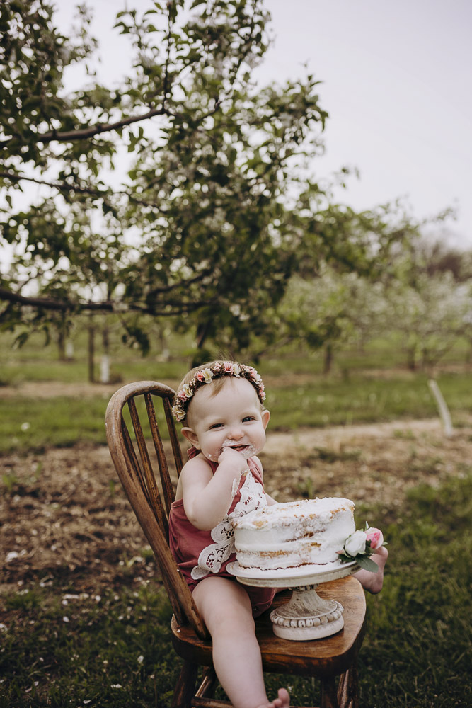 Sitting in a rustic chair enjoying her smash cake at her photography session.
