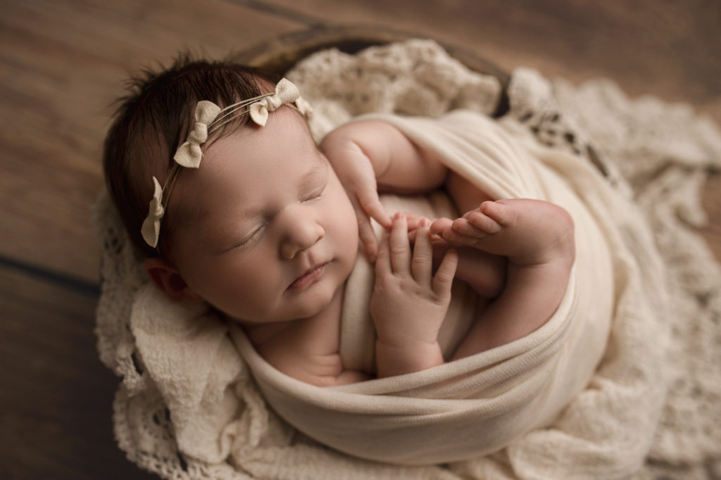 Baby girl posed in a wooden bowl with soft cream layer.
