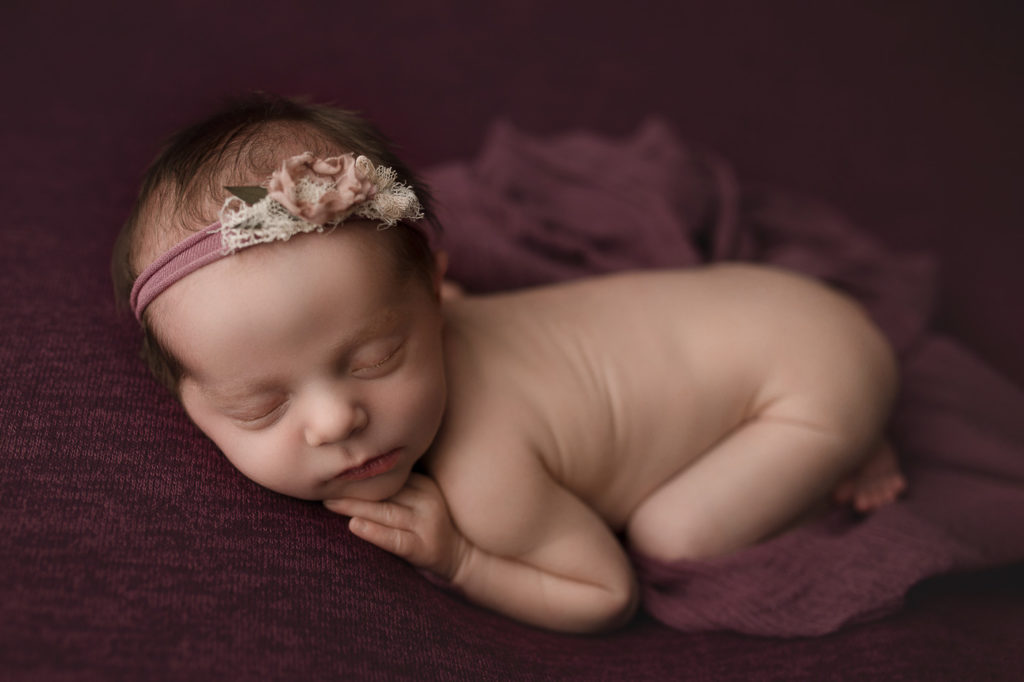 Adorable newborn girl on a maroon backdrop.