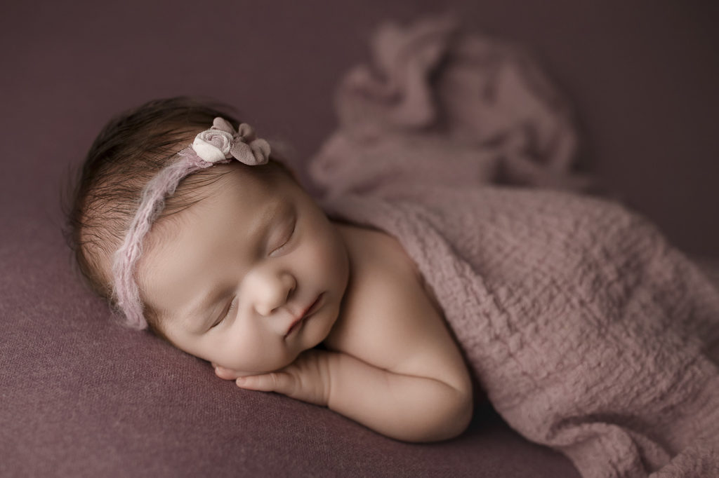 Sweet baby girl in side lying pose on berry back drop at her Lafayette newborn session.