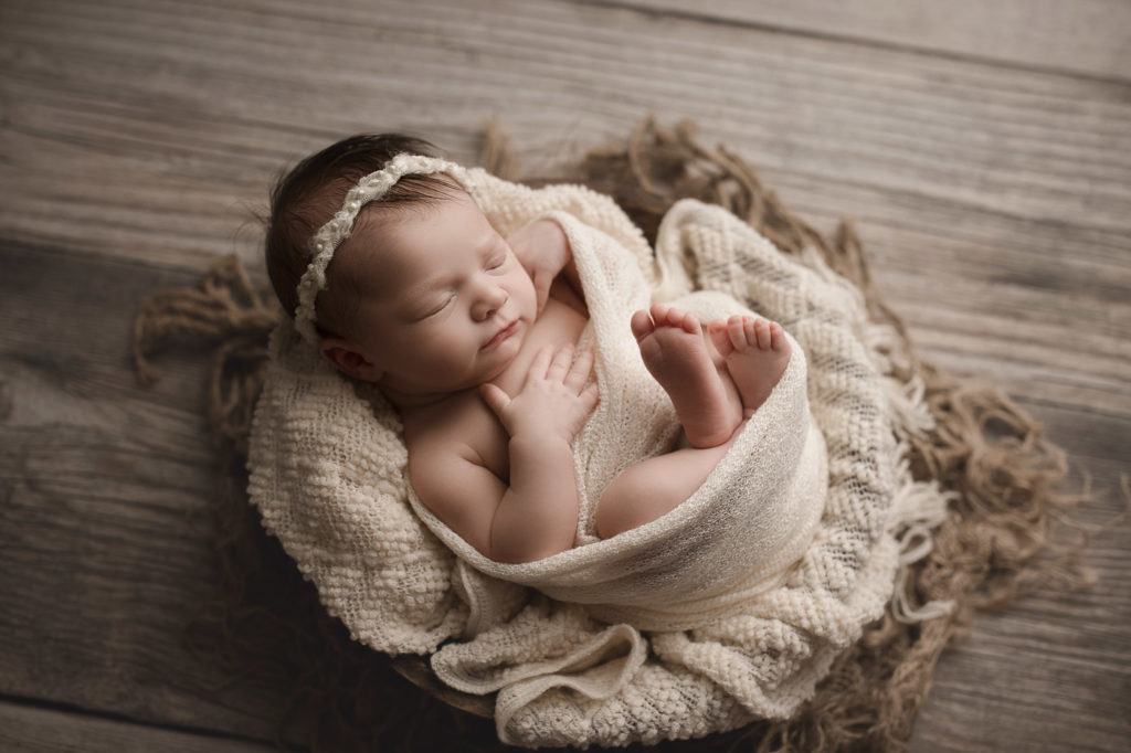 Baby girl posed so cute in a wooden bowl at her newborn photography session.