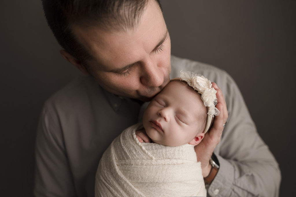 Dad giving his baby daughter a kiss on her foreahead during a newborn photography session.