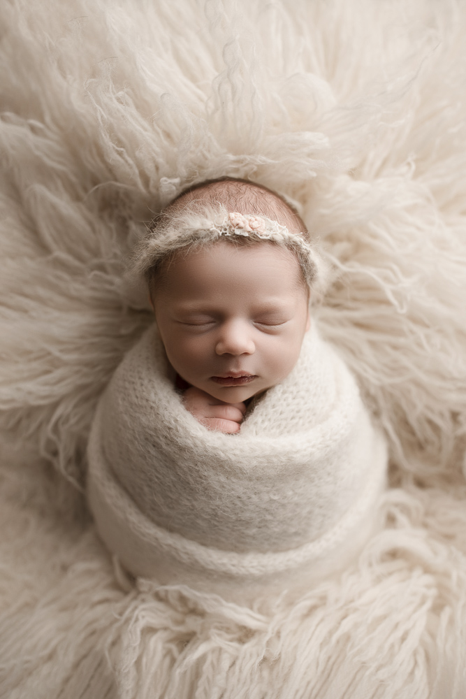 Sleeping newborn girl posed in a cream wrap and headband during her newborn session in Indiana.