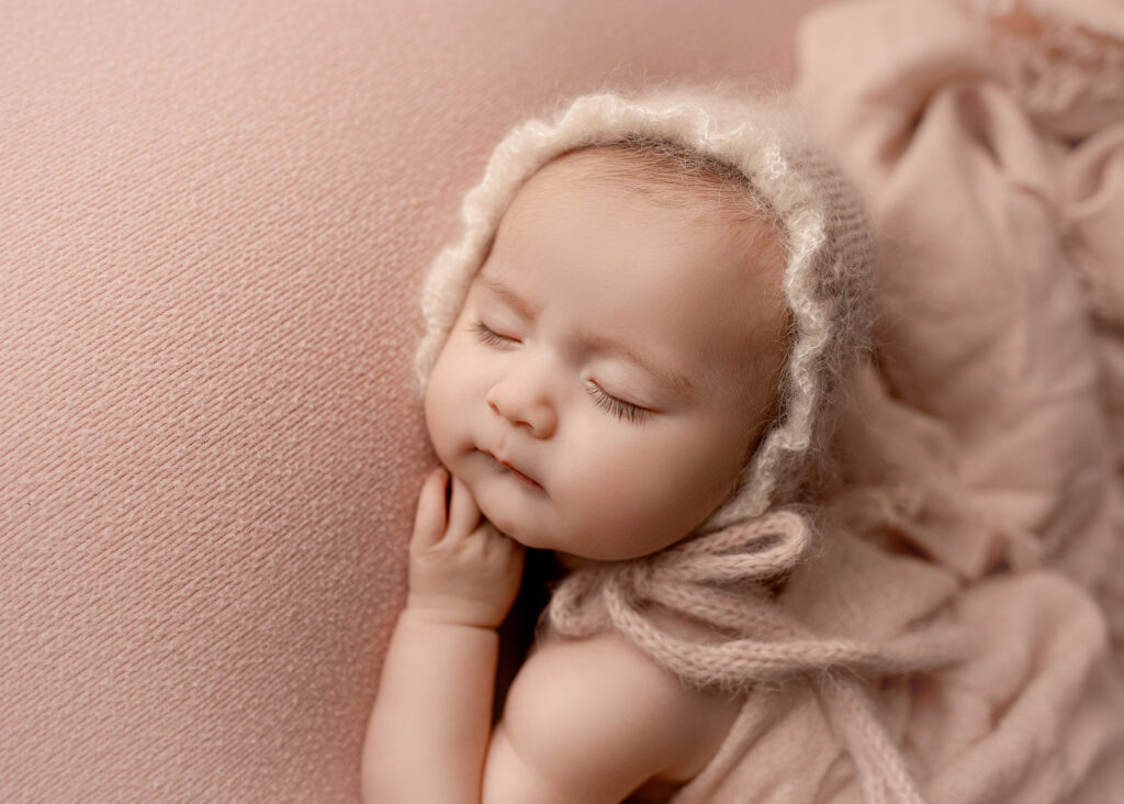 Precious sleeping baby in an adorable knit bonnet at her newborn studio session.